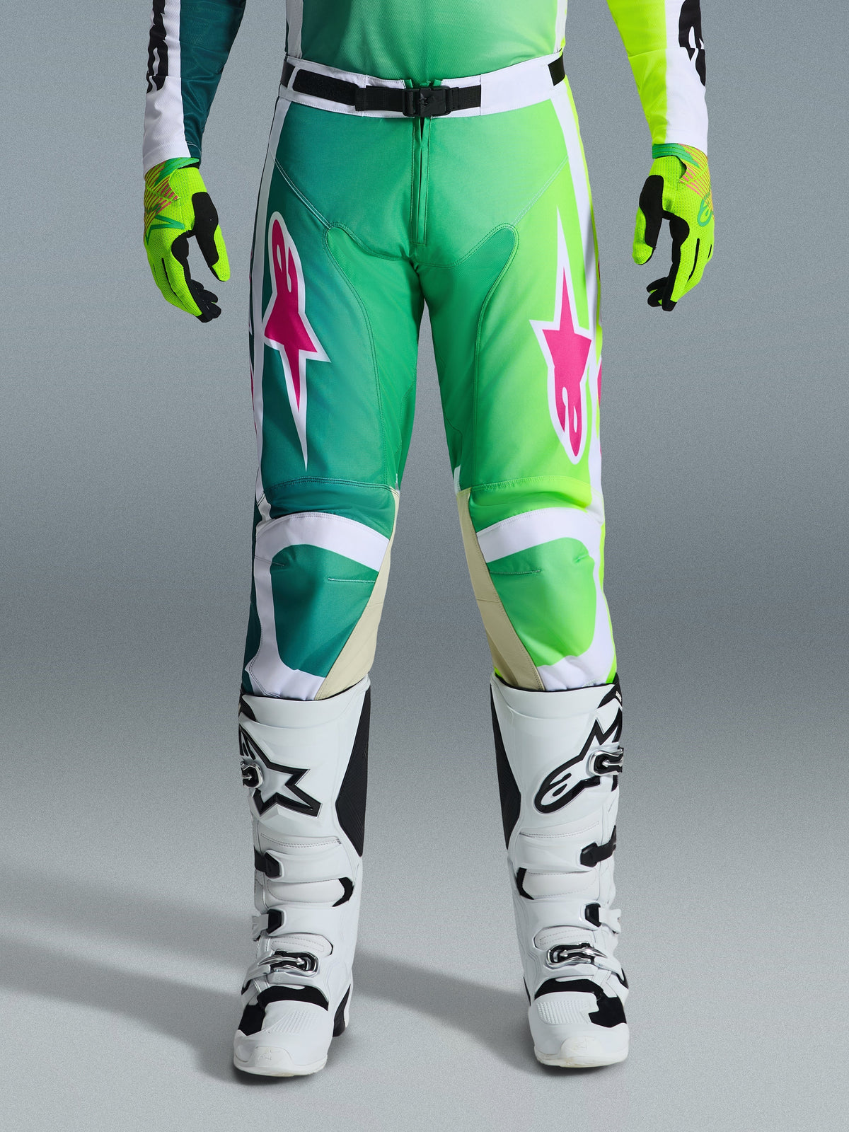Alpinestars 2026 Racer Portl Pants, Motocross Pants, Green White and Black with pink star logos, worn with white and black boots and lime green gloves, featuring a gradient design and ergonomic fit for off-road racing