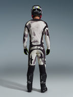 Motocross rider from behind wearing the 2026 Racer Lahnd Jersey and matching pants in Sand Camo, featuring a cream and grey abstract pattern with black panels, 'astars' branding on the pants, paired with black Alpinestars boots and a black helmet for a complete off-road racing look.