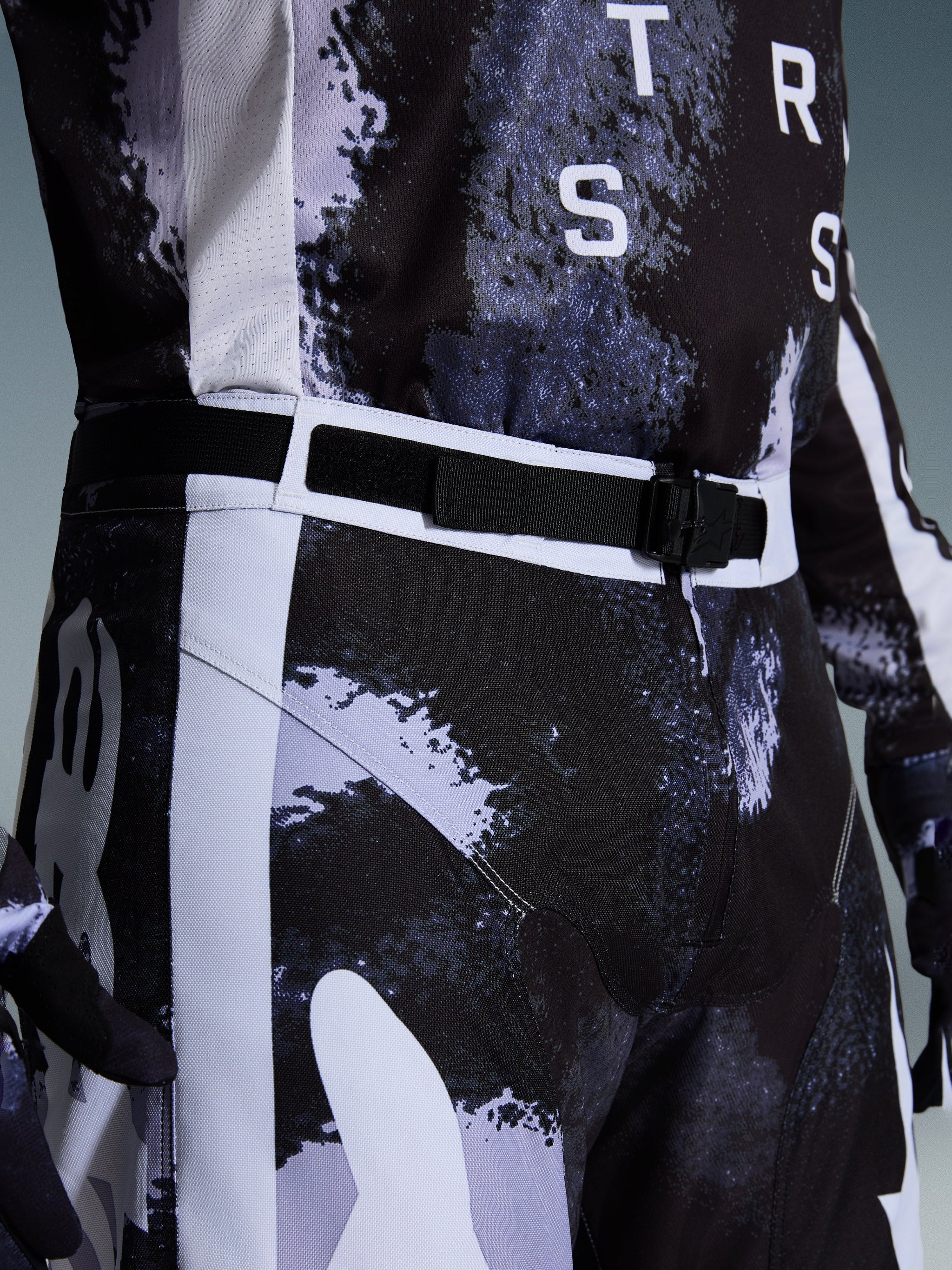 Alpinestars 2026 Racer Lahnd Pants, Motocross Pants in Iron Camo, close-up view of the adjustable waist belt and SX2 magnetic buckle, featuring a gray and black camouflage pattern and durable 600D polyfabric construction.
