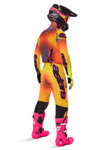 Motocross rider from a rear view wearing Alpinestars 2025 Supertech Lipan Pants, Yellow and Pink gradient, styled with matching jersey, bright pink boots, and a black helmet with pink accents, professional coordinated outfit for off-road racing.