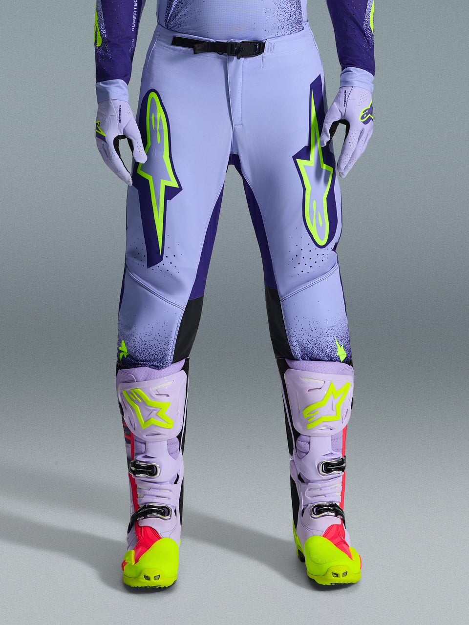Alpinestars 2026 Supertech Scenz Pants, Motocross Pants, Purple Yellow Fluo, featuring large neon yellow logos on the thighs, worn with matching purple and yellow motocross boots and gloves, athletic-fit performance design for off-road racing