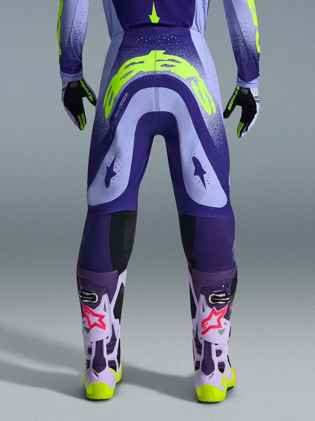 Alpinestars 2026 Supertech Scenz Pants, Motocross Pants, Purple and Yellow Fluo, rear view showing large yellow logo on seat, worn with matching jersey, gloves, and protective boots, athletic fit for professional motocross racing.