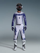 Motocross rider wearing Alpinestars 2026 Supertech Scenz gear set, Light Gray and Dark Blue, including a jersey and pants with matching blue gloves, white and black boots, and a black helmet with white goggles, coordinated outfit for professional off-road racing