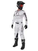 Alpinestars 2025 Racer Hollow Pants, Motocross Pants, Light Camo Brown, shown as part of a complete racing kit with a white jersey, black helmet, and black boots, featuring reinforced black knee panels and a subtle camouflage design.