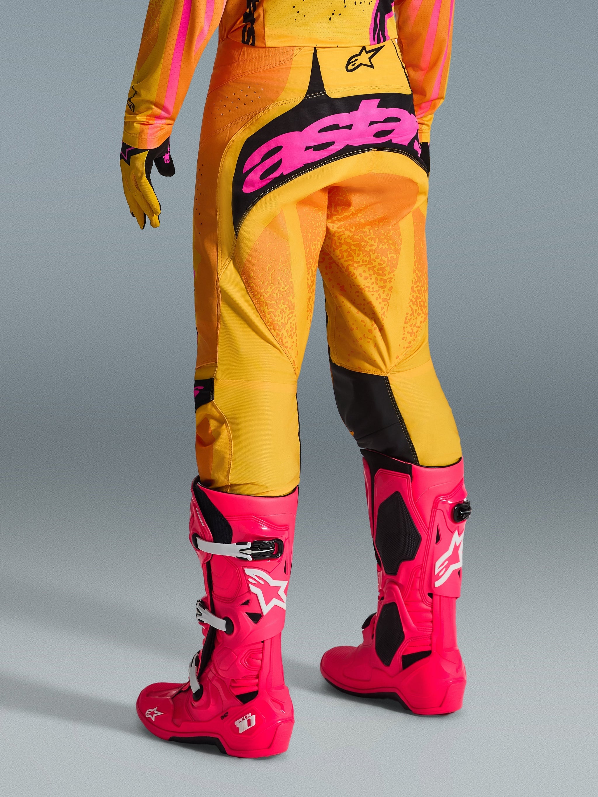 Alpinestars 2026 Techstar Nomur Pants, Motocross Pants, Orange Yellow and Pink, rear view, featuring large pink 'astars' branding on the seat, paired with bright pink Tech 10 boots and matching jersey, performance racing gear for motocross