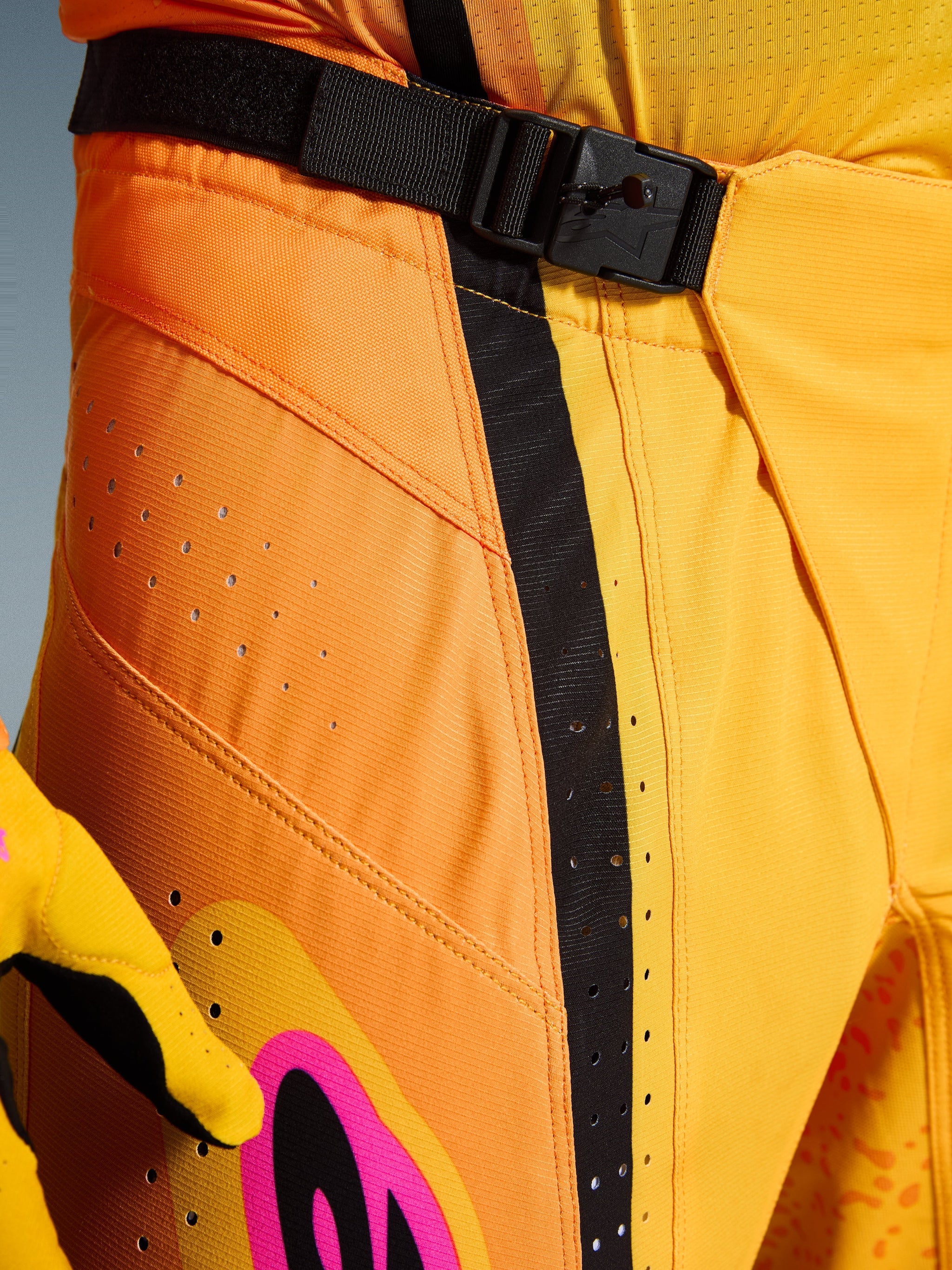 Alpinestars 2026 Techstar Nomur Pants, Motocross Pants, Orange Yellow Pink, close-up of the waist area featuring the SX2 magnetic buckle closure, black adjustment strap, and laser-cut ventilation perforations on durable ripstop material