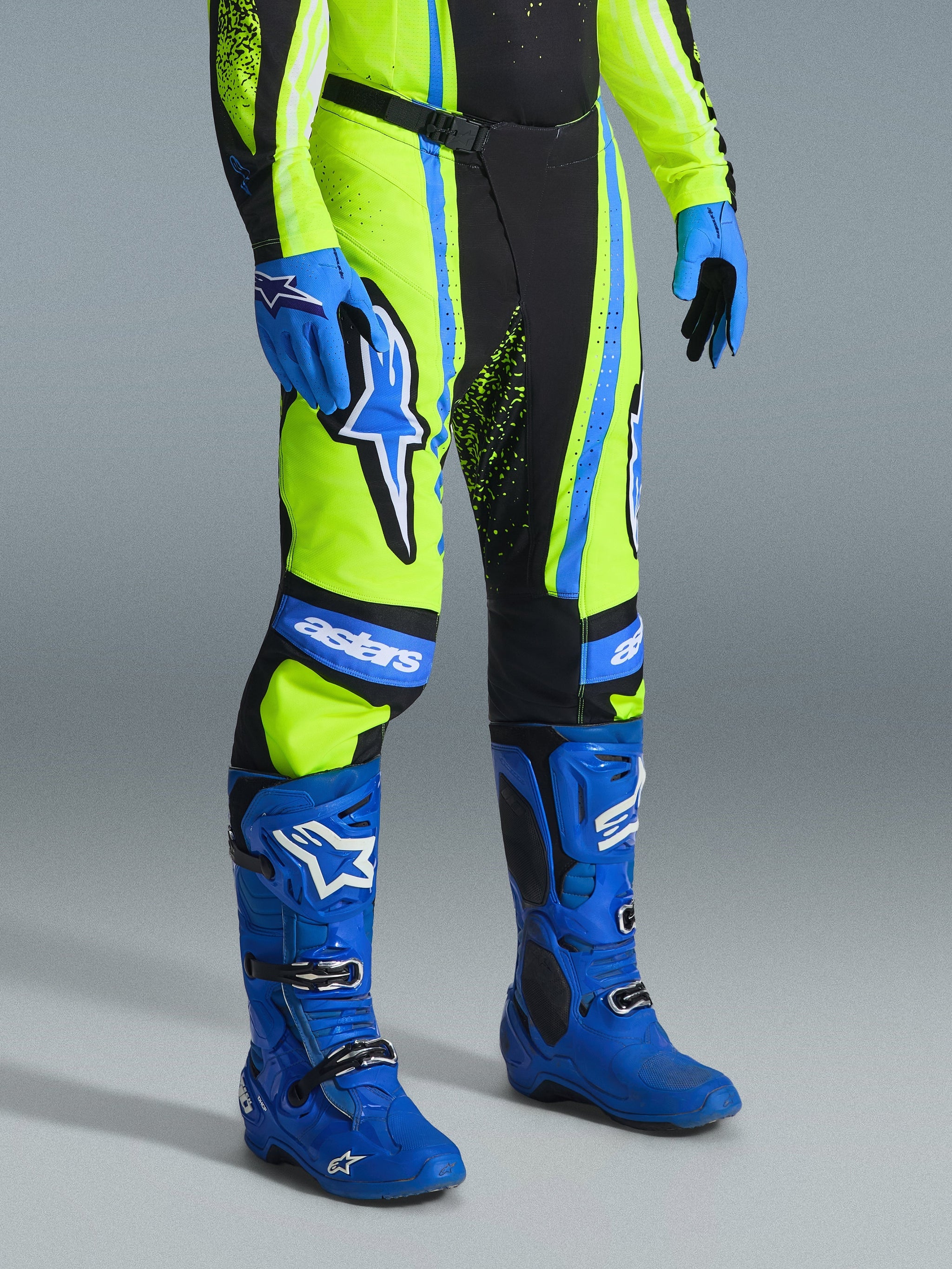 Alpinestars 2026 Techstar Nomur Pants, Motocross Pants, Yellow Fluo, Dark Navy, and UCLA Blue, worn with matching blue boots and gloves, featuring bold white logos and reinforced panels, professional off-road racing attire