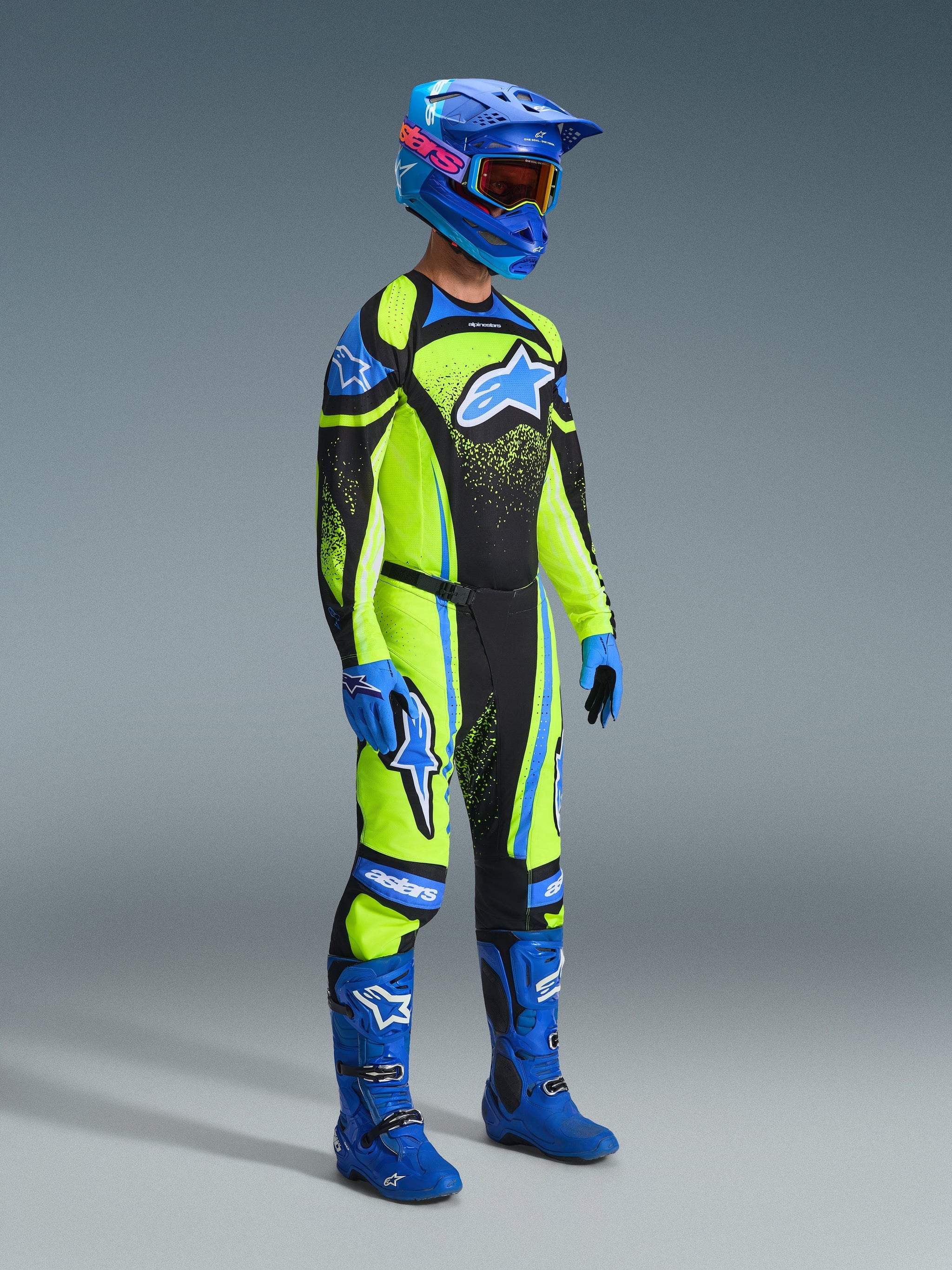 Motocross rider wearing complete racing gear, Yellow fluo jersey with dark navy and blue accents, Alpinestars 2026 Techstar Nomur Pants in matching colors, blue helmet with goggles, blue and black boots, blue gloves, coordinated outfit for off-road racing