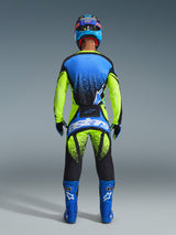 Motocross rider from the back wearing Alpinestars 2026 Techstar Nomur Pants, Yellow Fluo and UCLA Blue with Dark Navy accents, matching jersey and blue boots, featuring bold Astars branding on the seat and a speckled graphic design.