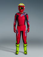 Motocross rider wearing complete racing gear, Alpinestars 2026 Fluid Grid Pants in Red Black and Purple, matching red and black jersey with Alpinestars logo, red helmet with fluorescent yellow accents, fluorescent yellow boots, and red gloves, full gear set for off-road motocross racing