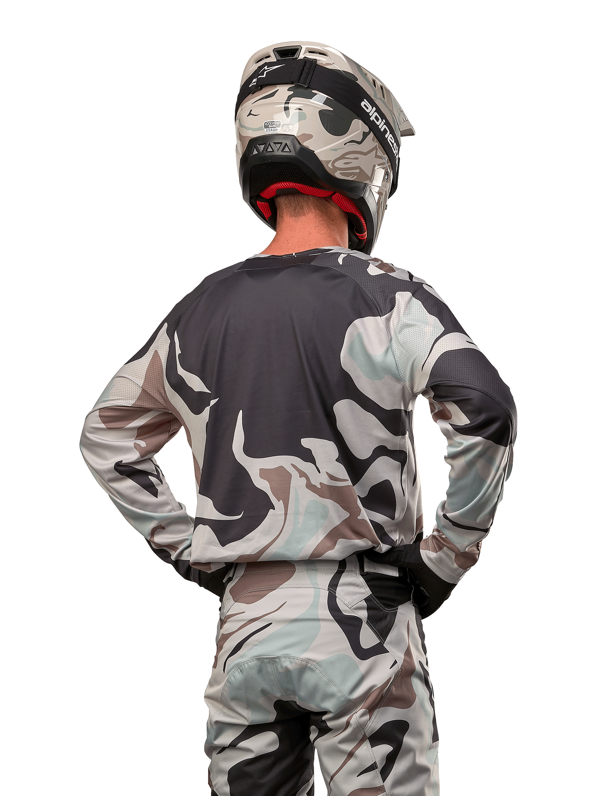 Motocross rider seen from behind wearing the Alpinestars 2024 Racer Tactical Jersey in Iron Camo Dust Gray, matching camouflage pants and helmet, hands on hips, coordinated off-road racing gear.