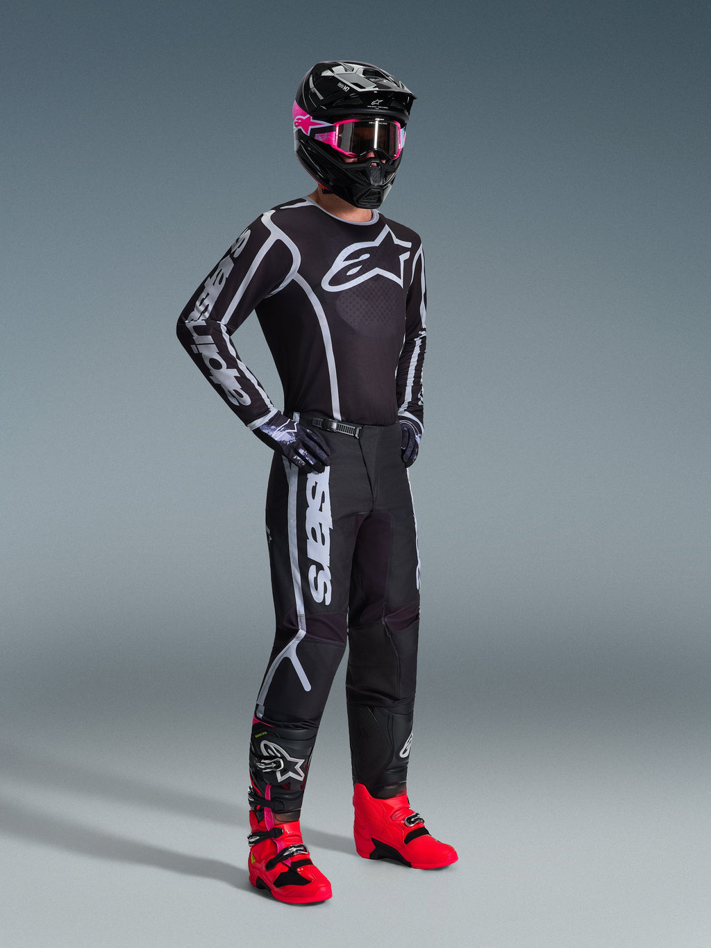 Alpinestars 2026 Fluid Apex Pants, Motocross Pants, Black and Gray, worn with matching black and white jersey, black helmet with pink goggles, and bright red boots, featuring bold white branding on the legs and a sport-fit design for off-road racing.