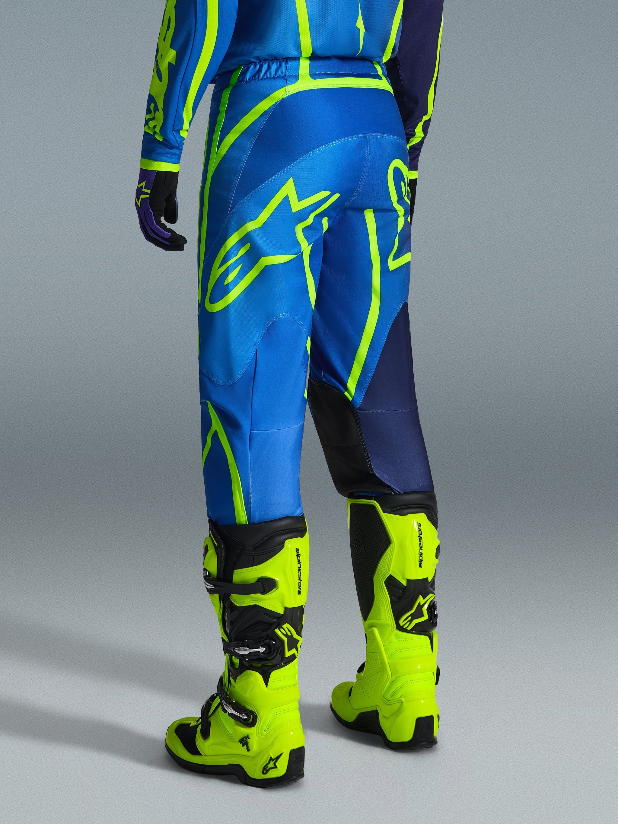 Alpinestars 2026 Fluid Apex Pants, Motocross Pants, Blue and Yellow Fluo, back view of rider wearing matching gear and fluorescent yellow boots, featuring bold Alpinestars logos and ergonomic design