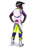 Motocross rider wearing Alpinestars Limited Edition Supertech Dirt Studios® Pants in White Purple and Yellow Fluo, seen from the back with matching jersey, boots, and black carbon helmet, professional off-road racing gear with bold graphics and neon accents.