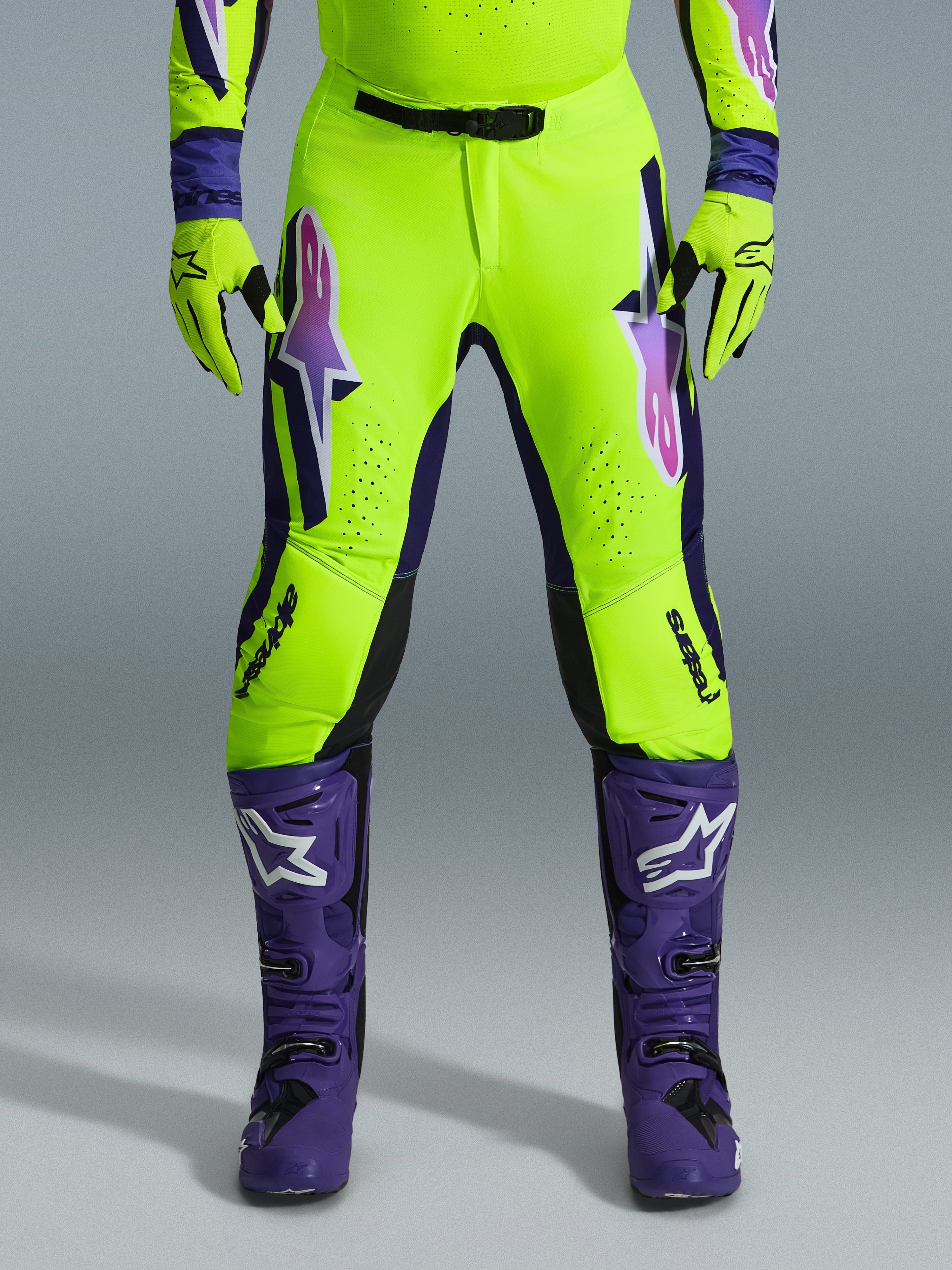 Alpinestars 2026 Supertech Vista Pants, Motocross Pants, Fluorescent Yellow Purple and Black, worn with matching gloves and purple boots, featuring large gradient logos on thighs, perforated zones for ventilation, and a professional athletic design for off-road racing