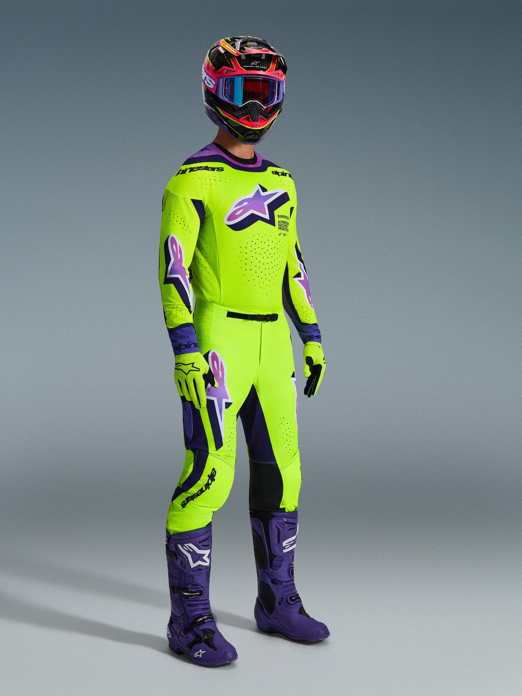 Motocross rider wearing the 2026 Supertech Vista Jersey, Bright Yellow with purple and black accents, matching yellow motocross pants, purple boots, and yellow gloves, multicolored helmet with blue goggles, high-performance racing gear for off-road competition