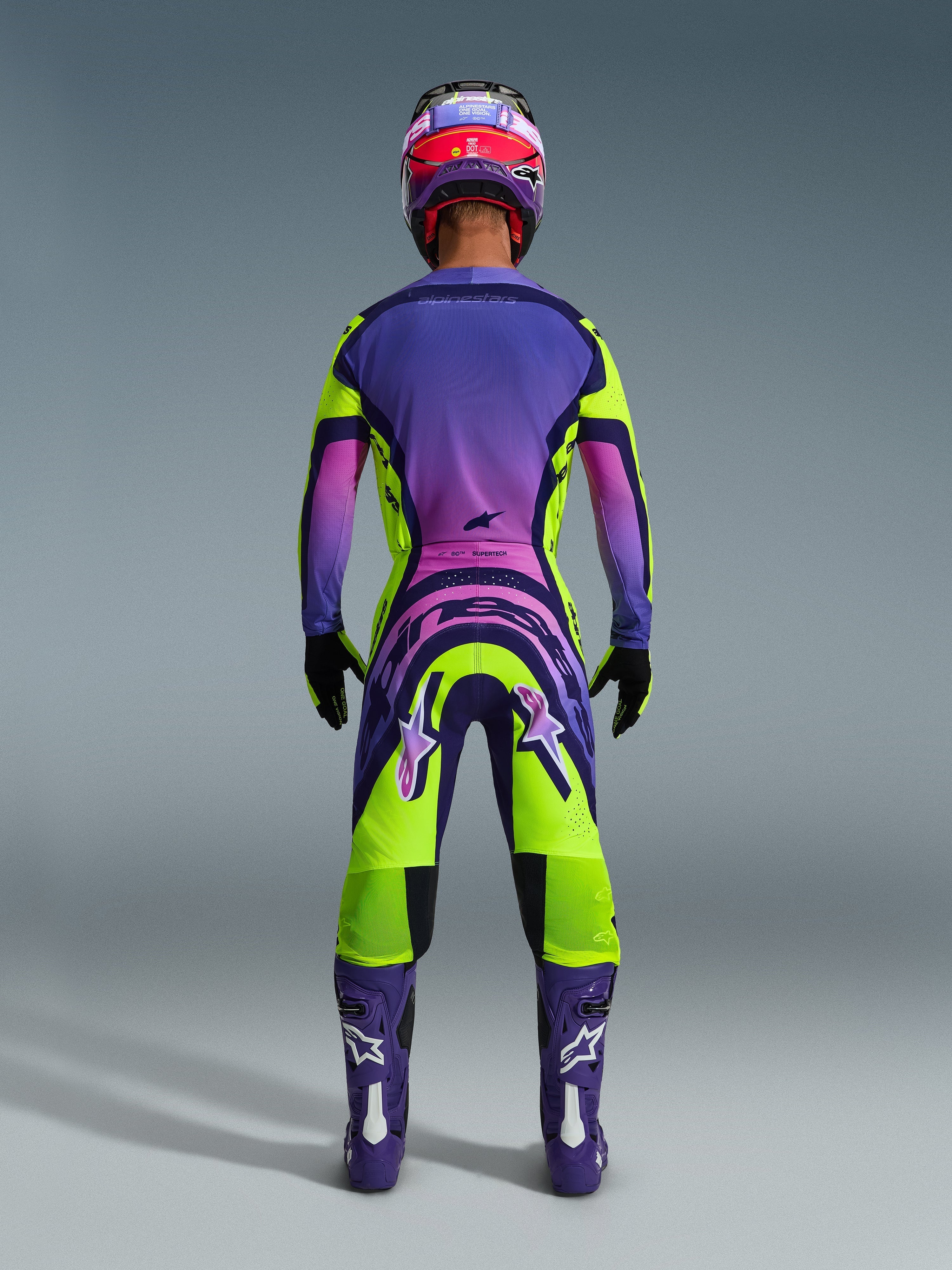 Alpinestars 2026 Supertech Vista Pants, Motocross Pants, Yellow Purple and Black, rear view of a motocross rider in a complete racing gear set with a purple gradient jersey and purple boots, vibrant athletic design for professional off-road racing
