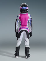Youth motocross rider seen from the back wearing Alpinestars 2026 Youth Fluid Grid Pants, Black Light Gray and Purple colorway, matching white and pink jersey with blue logos, black helmet with pink accents, black and white boots, full gear set for off-road racing