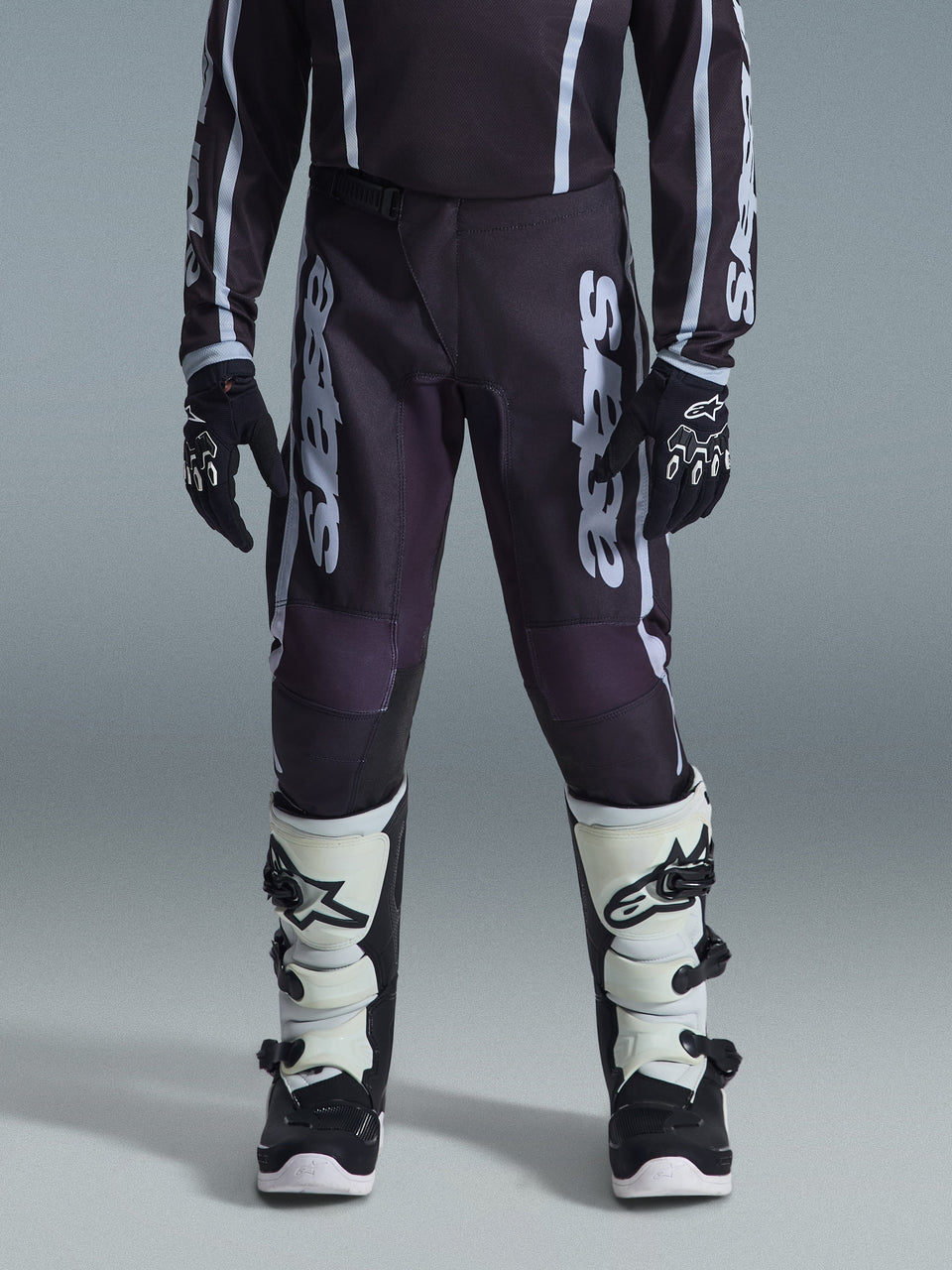 Alpinestars 2026 Youth Fluid Apex Pants, Motocross Pants, Black and Gray, featuring white 'Astars' vertical branding on thighs, worn with black gloves and white and black boots, durable material for youth off-road racing