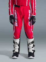 Alpinestars 2026 Youth Fluid Apex Pants, Motocross Pants, Red and White, shown on a rider with matching red jersey, black gloves, and white and black boots, featuring large white vertical Alpinestars branding and black inner knee reinforcement for off-road performance