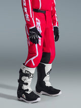 Alpinestars 2026 Youth Fluid Apex Pants, Motocross Pants, Red and White, worn with black gloves and white and black boots, featuring bold white branding, black knee panels, and a secure ratchet waist closure, designed for off-road racing
