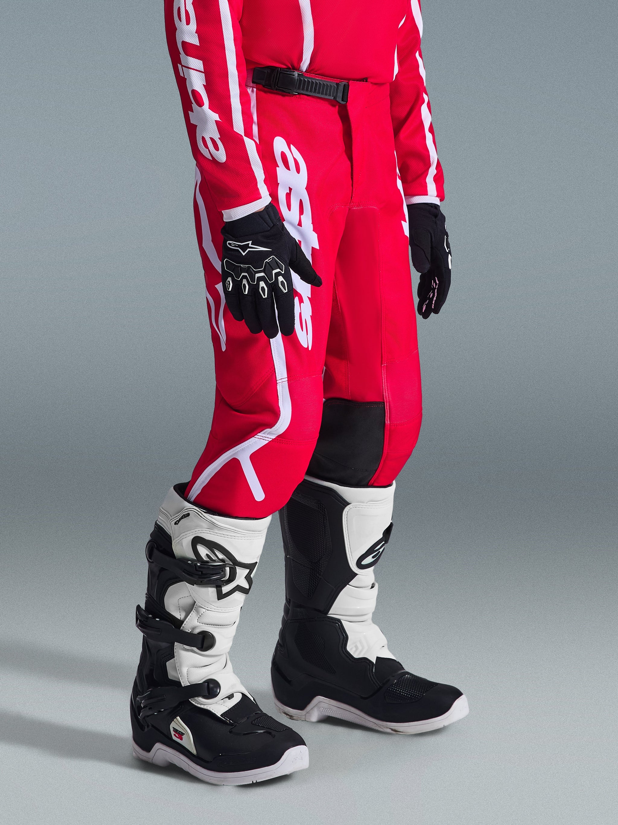 Alpinestars 2026 Youth Fluid Apex Pants, Motocross Pants, Red and White, worn with black gloves and white and black boots, featuring bold white branding, black knee panels, and a secure ratchet waist closure, designed for off-road racing