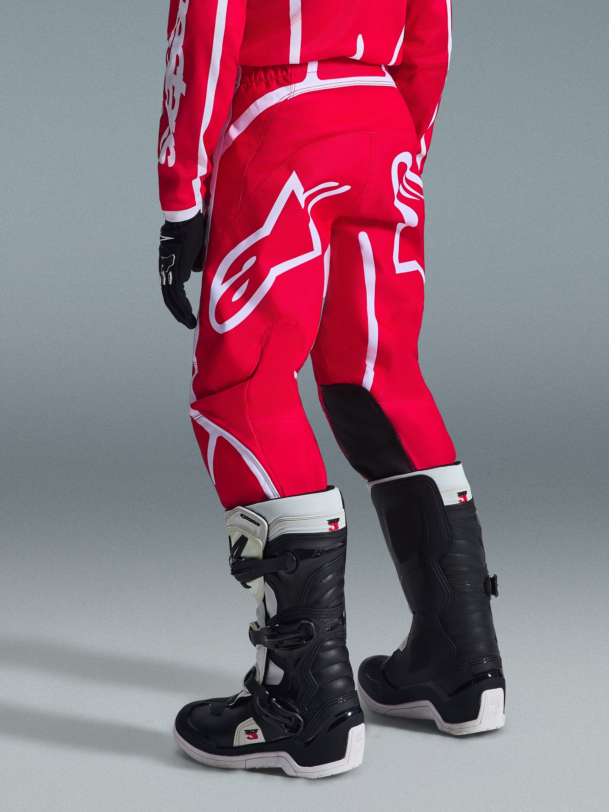 Alpinestars 2026 Youth Fluid Apex Pants, Motocross Pants, Red and White, rear view, featuring bold white branding and black inner knee panels, worn with matching jersey and black and white motocross boots