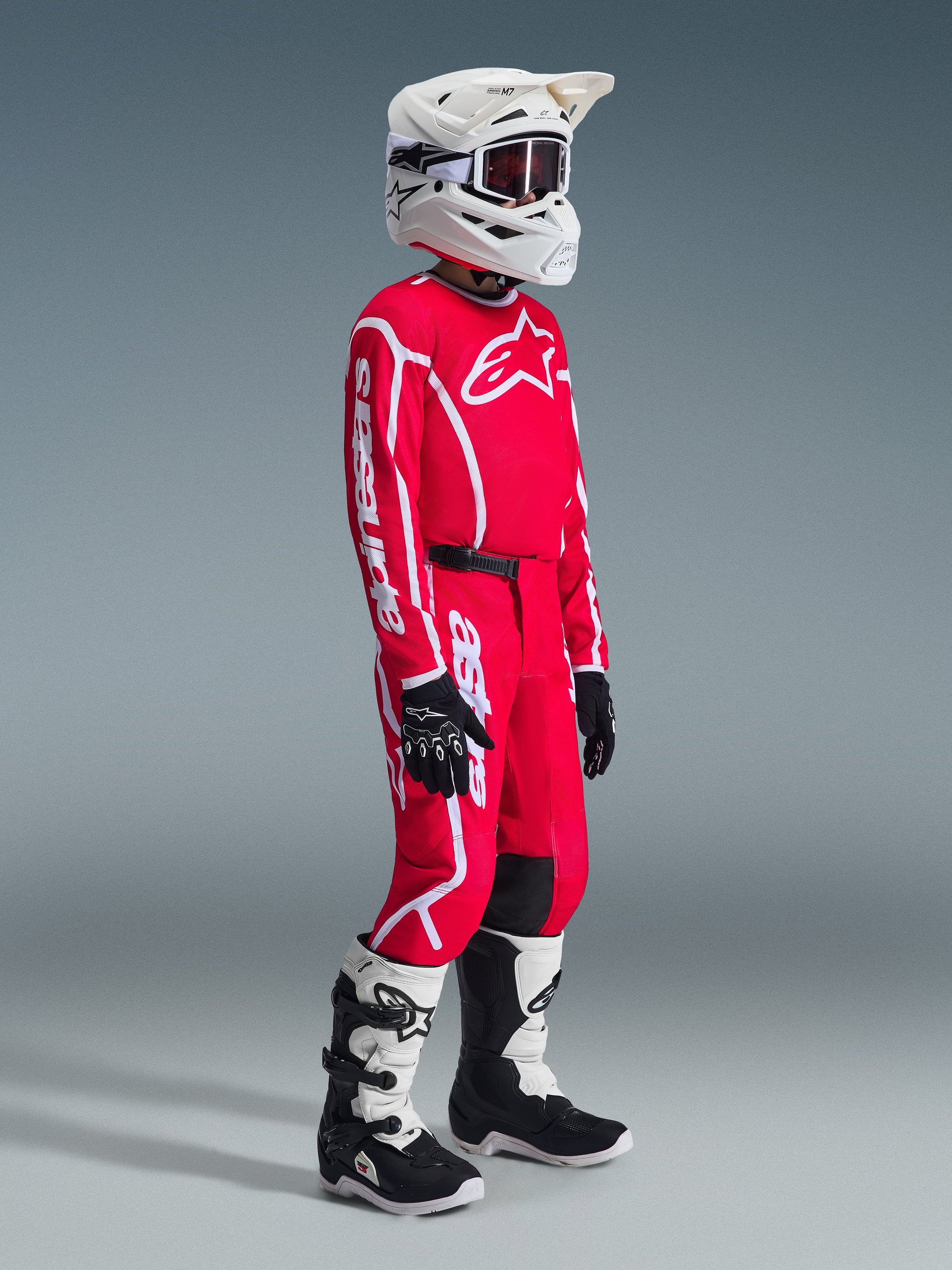 Alpinestars 2026 Youth Fluid Apex Pants, Motocross Pants, Red and White, worn by a rider in full racing gear including a matching jersey, white helmet, and black and white boots, featuring bold white logos and durable materials for off-road racing