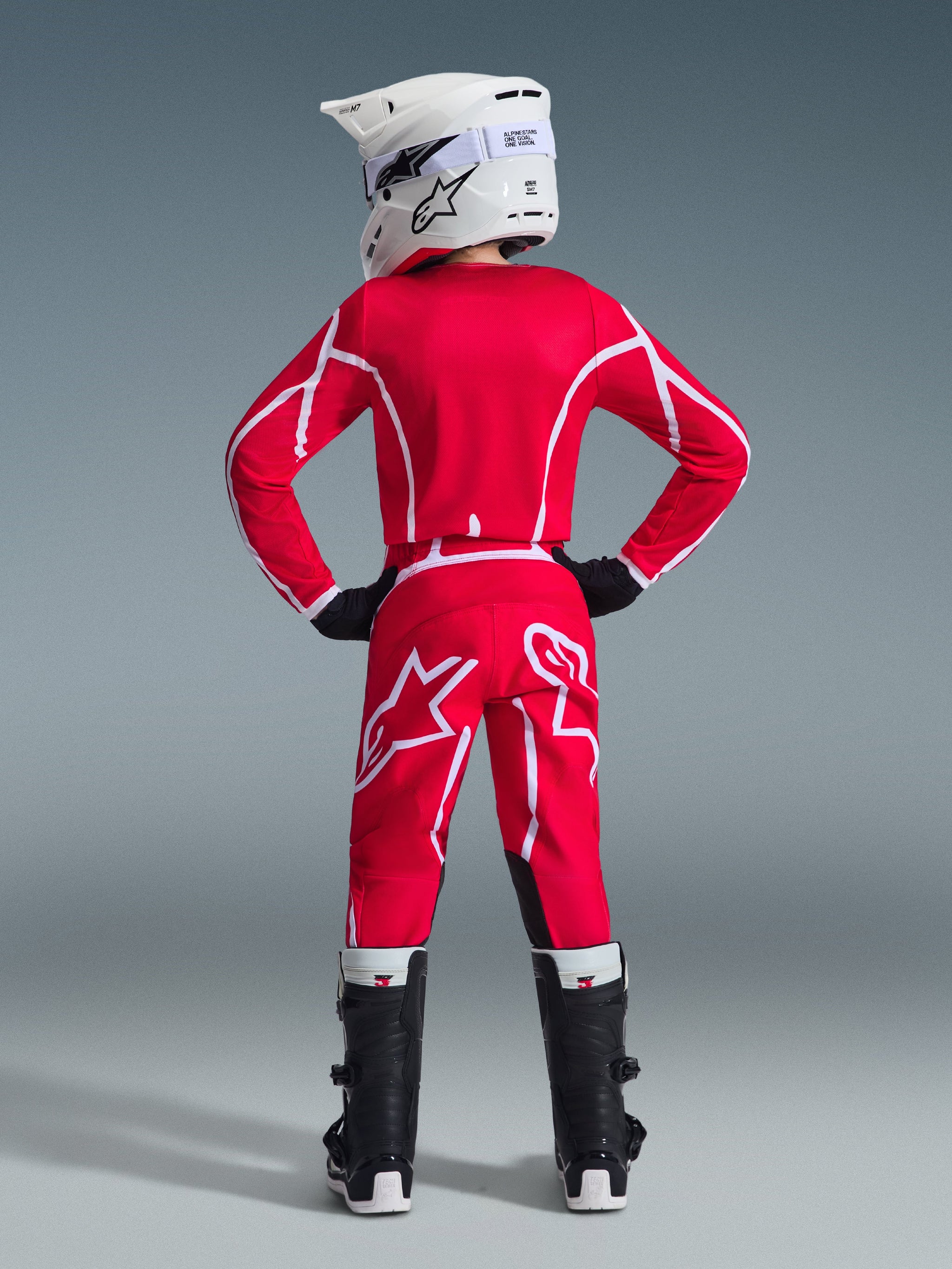 Alpinestars 2026 Youth Fluid Apex Pants, Motocross Pants, Red and White, rear view showing matching jersey, white helmet, and black and white boots, featuring bold white geometric patterns and large Alpinestars logo on the back, complete youth racing gear set.