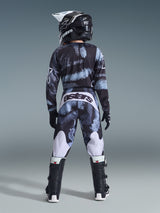 Alpinestars 2026 Youth Fluid Lahnd Pants, Motocross Pants, Iron Camo with blue and grey tones, rear view of rider wearing matching gear set including helmet and boots, white accents on legs and 'astars' logo on back.