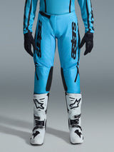Alpinestars 2026 Woman Stella Fluid Apex Pants, Motocross Pants, Bright Cyan and Black, vertical black branding on thighs, black reinforced inner knee panels, shown with white and black motocross boots and black gloves, professional off-road gear for women