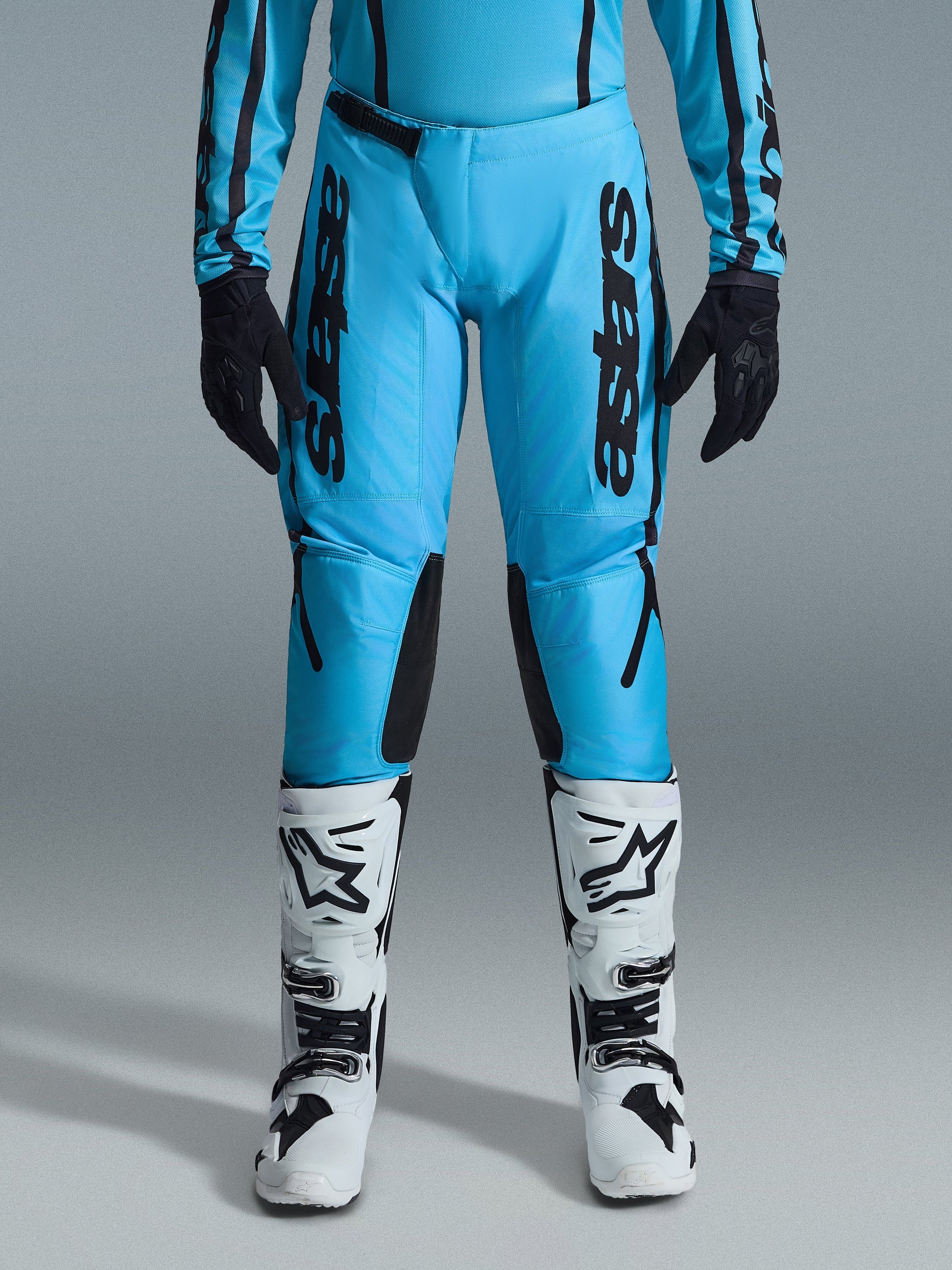 Alpinestars 2026 Woman Stella Fluid Apex Pants, Motocross Pants, Bright Cyan and Black, vertical black branding on thighs, black reinforced inner knee panels, shown with white and black motocross boots and black gloves, professional off-road gear for women