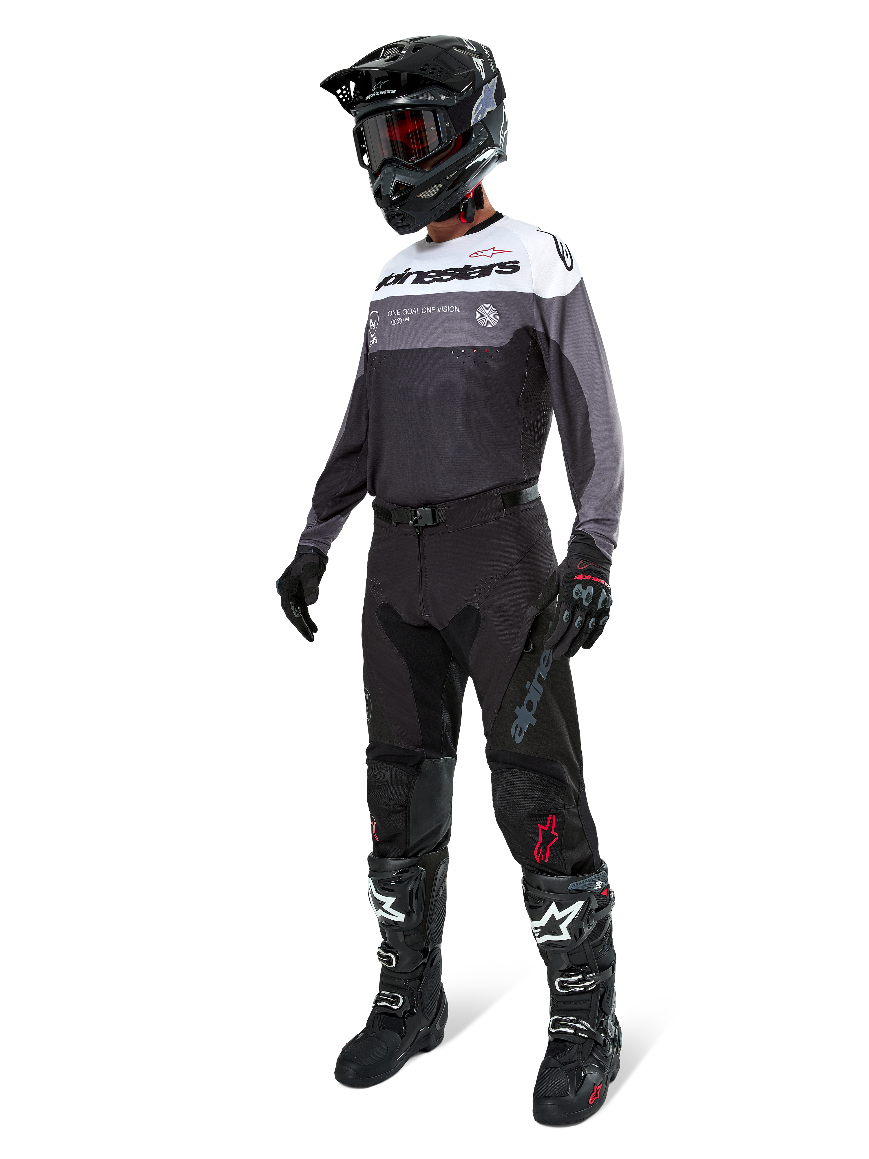 Alpinestars Pro-Dura Jersey in Black Magnet White, worn by a motocross rider in full gear including black pants, black helmet with goggles, and black and white boots. The jersey features a technical color-blocked design with white, grey, and black panels, engineered for enduro and off-road performance.