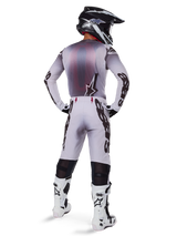 Motocross rider from behind wearing Alpinestars 2025 Supertech Maker Pants in Silver and Black, matching long-sleeve jersey, black and white helmet, and white and black boots, featuring bold black branding on the legs, professional off-road racing gear.