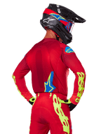 Rear view of a motocross rider wearing the Alpinestars 2025 Supertech Maker Gear Set in Red, featuring a red jersey with neon yellow branding on the sleeves, matching red pants, a black helmet with blue and red accents, and coordinating black and yellow gloves.