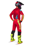 Motocross rider from a rear view wearing the Alpinestars 2025 Supertech Maker Gear Set, Bright Red jersey with yellow fluo branding, matching red pants with yellow accents, black helmet with red and blue details, fluo yellow boots, coordinated professional racing outfit for off-road performance.