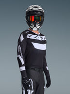 Motocross rider wearing the 2026 Racer Air Riway Jersey, Black and White jersey with 'astars' logo, matching black and white helmet with orange mirrored goggles, black motocross pants and gloves, coordinated outfit for off-road racing