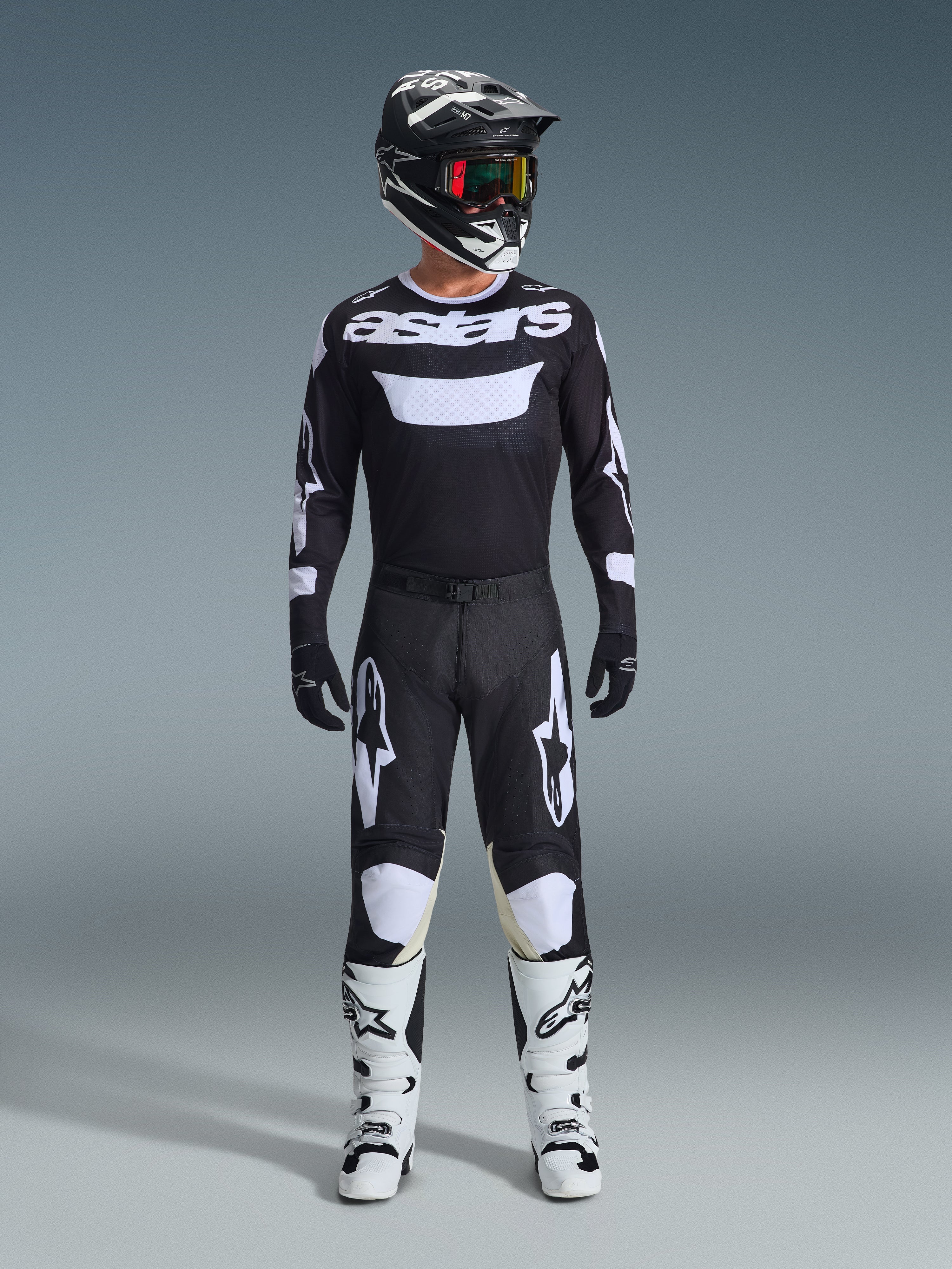 Motocross rider wearing complete racing gear, Alpinestars 2026 Racer Air Riway Jersey in Black and White with 'astars' branding on chest, matching black pants with white accents, white motocross boots, and black and white helmet with goggles, coordinated professional off-road racing outfit