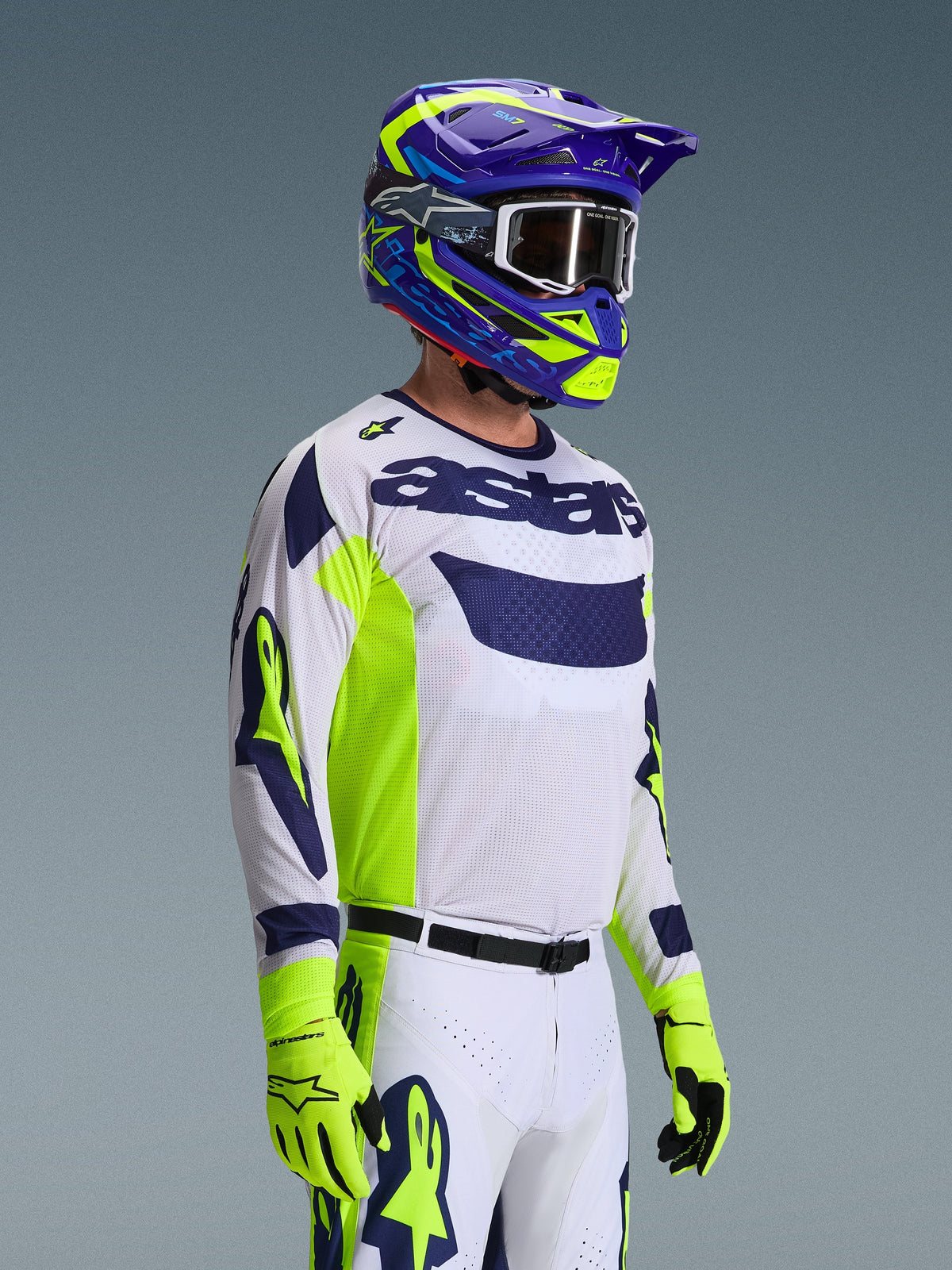 Motocross rider wearing the Alpinestars 2026 Racer Air Riway Jersey, Light Gray with Yellow Fluo and Blue accents, paired with a matching blue and yellow helmet and fluo yellow gloves, featuring breathable mesh construction and professional race styling for off-road performance.