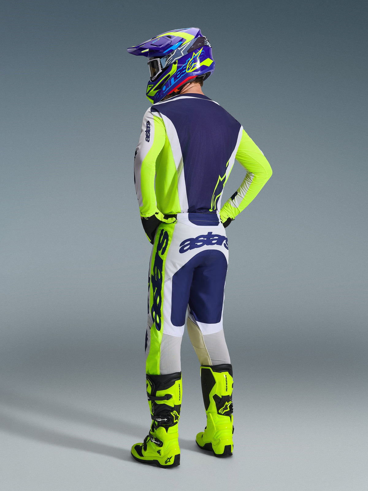 Motocross rider from behind wearing the 2026 Racer Air Riway Jersey in Light Gray Yellow Fluo Blue, matching pants with bold branding, bright yellow fluo motocross boots, and a blue and yellow helmet, complete off-road racing gear set.