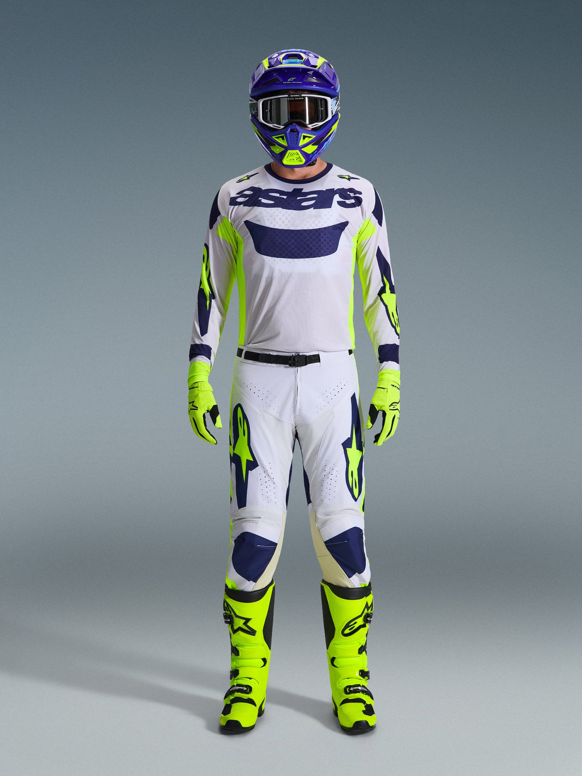 Motocross rider wearing complete racing gear, light gray Racer Air Riway Jersey with neon yellow and blue accents, matching white and yellow pants, neon yellow boots and gloves, purple and yellow helmet, professional outfit for off-road racing