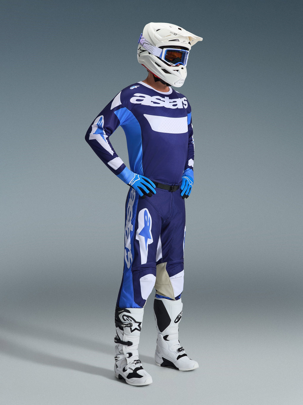 Motocross rider wearing the Alpinestars 2026 Racer Riway Gear Set in UCLA Blue and White, featuring a blue and white jersey with 'astars' branding, matching pants, a white helmet with blue goggles, and white off-road boots, complete racing outfit for motocross.