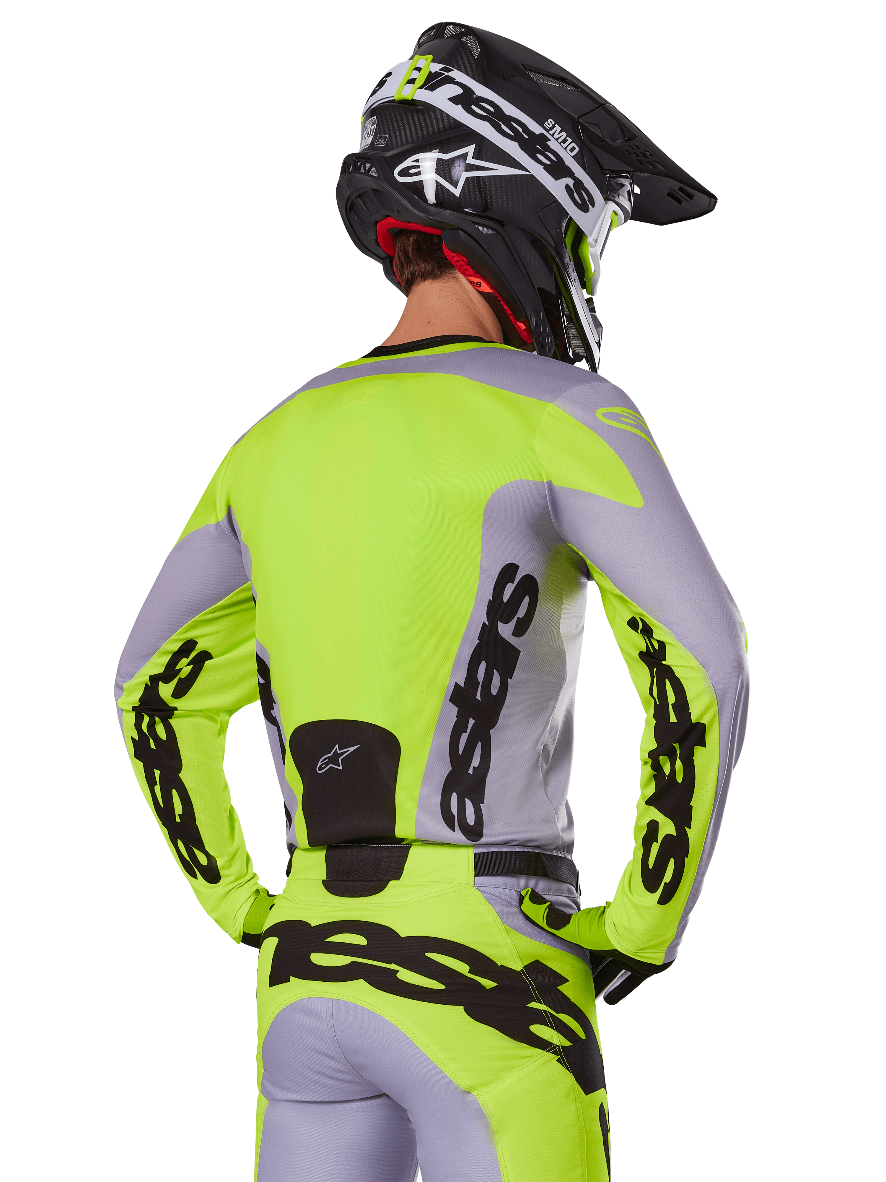 Motocross rider from behind wearing the Alpinestars 2025 Racer Veil Jersey in Gray and Yellow Fluo, featuring prominent 'astars' branding on the back and sleeves, paired with matching pants and a black helmet for a complete racing look.