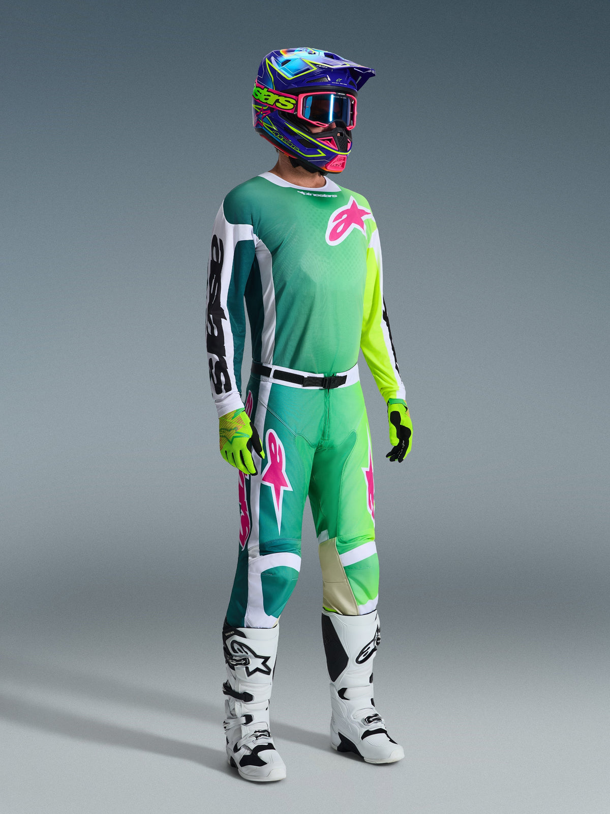 Motocross rider wearing complete racing gear, 2026 Racer Portl Jersey in green with white and black sleeves and pink logo, matching green pants with pink accents, multi-colored helmet with goggles, white and black boots, and green gloves, coordinated outfit for off-road racing