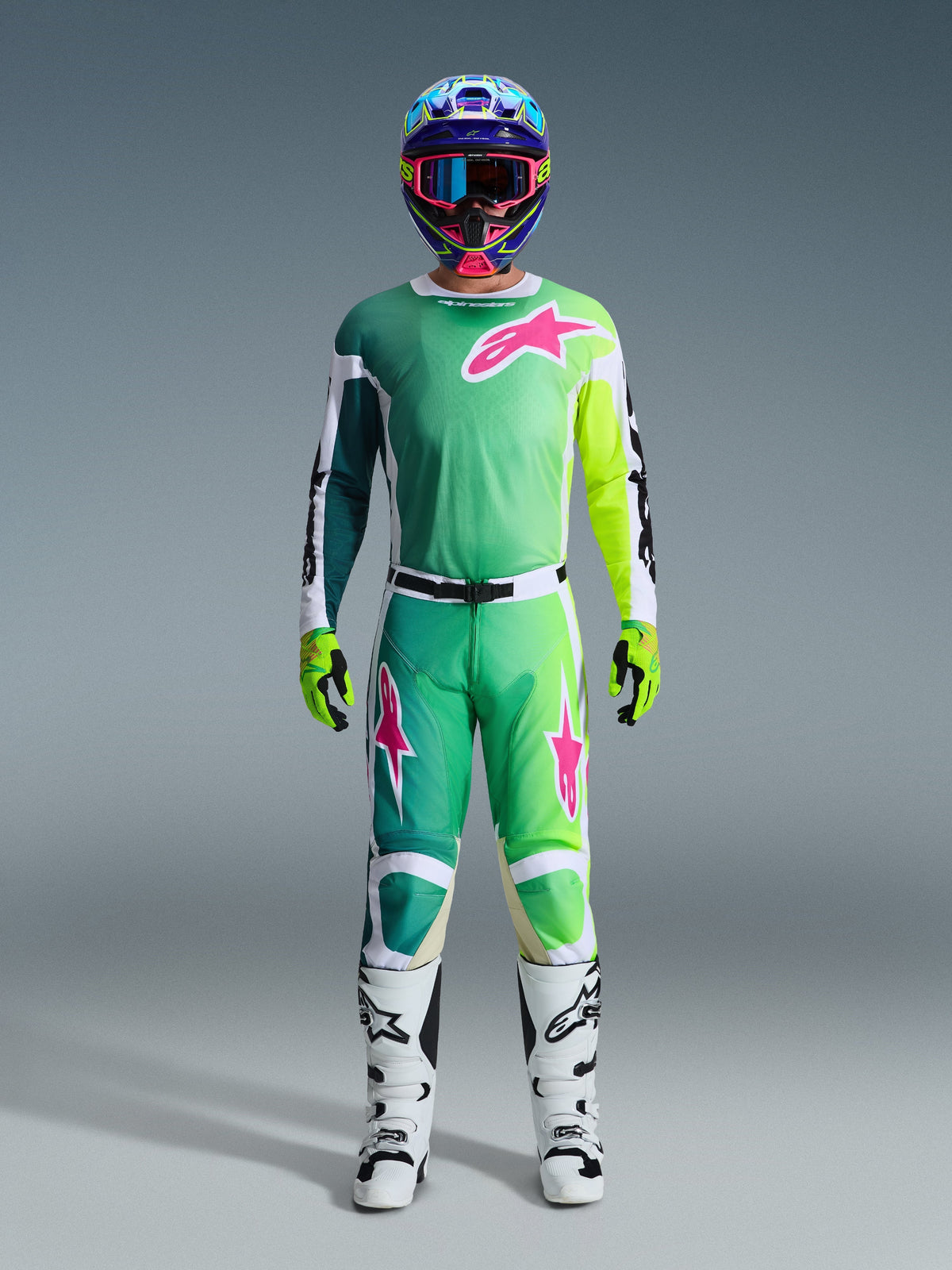 Motocross rider wearing the 2026 Racer Portl Jersey in Green, White, and Black, featuring vibrant pink and lime green accents and a large pink star logo on the chest, paired with matching pants, a colorful helmet, lime green gloves, and white motocross boots, complete racing gear set.