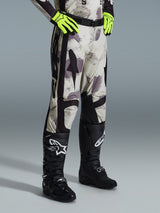 Alpinestars 2026 Racer Lahnd Pants, Motocross Pants, Sand Camo, worn with neon yellow gloves and black motocross boots, featuring an abstract camouflage pattern with black side panels, ergonomic off-road design