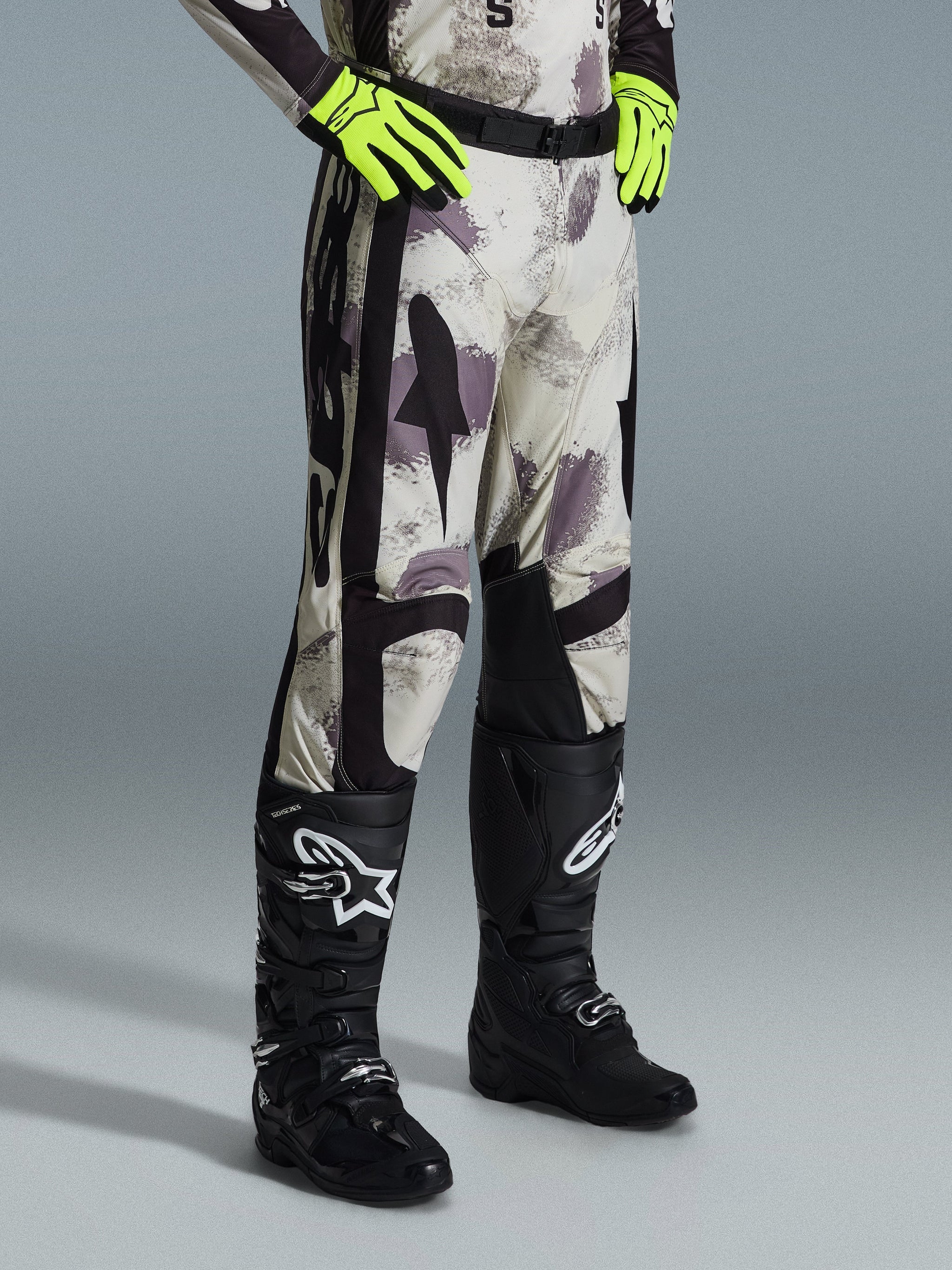 Alpinestars 2026 Racer Lahnd Pants, Motocross Pants, Sand Camo, worn with neon yellow gloves and black motocross boots, featuring an abstract camouflage pattern with black side panels, ergonomic off-road design