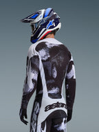 Alpinestars 2026 Racer Lahnd Gear Set, Motocross rider from behind wearing jersey and pants with black and white speckled graphic, paired with a blue and white Alpinestars helmet and black gloves, performance off-road racing gear