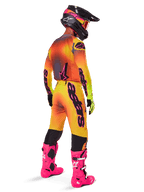 Motocross rider from behind wearing the Alpinestars 2025 Supertech Lipan Gear Set, yellow and orange gradient jersey with pink accents, matching pants, bright pink boots, and a black helmet with pink and yellow graphics, coordinated outfit for professional racing