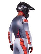 Motocross rider from behind wearing the Alpinestars 2025 Supertech Lipan Jersey in Gray Orange Fluo, featuring bold orange logos on the sleeves and back, paired with matching pants and a black helmet, professional racing outfit for off-road performance.